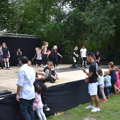 Tanzgruppe auf einer B&uuml;hne bei einer Auff&uuml;hrung, umgeben von Zuschauern auf der Wiese.