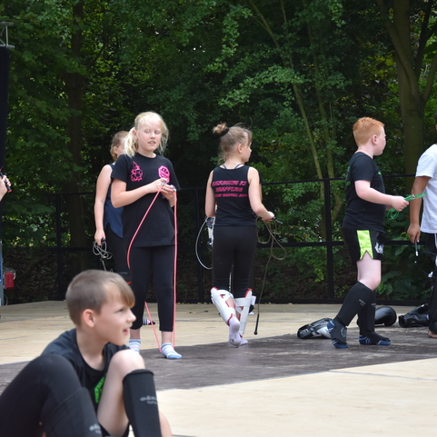 Gruppe von Kindern in Sportkleidung bei einer Trainingseinheit auf einer Freiluftb&uuml;hne, einige halten Springseile.