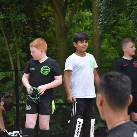 Vier Kinder in Sportkleidung stehen in einem Freiluftbereich, w&auml;hrend ein anderes Kind Ausr&uuml;stung vorbereitet.