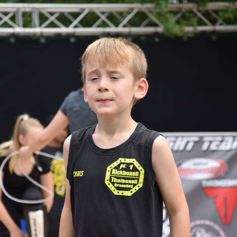 Ein junger K&auml;mpfer im sportlichen Outfit steht konzentriert auf einer Wettkampf-B&uuml;hne vor einem schwarzen Hintergrund.