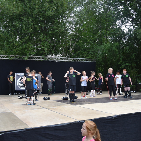 Kinder und Jugendliche in Sportkleidung &uuml;ben auf einer Freilichtb&uuml;hne vor einer Zuschauergruppe.