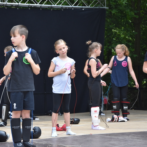 Gruppe von Kindern in Sportkleidung trainiert mit Springseilen auf einer B&uuml;hne im Freien.