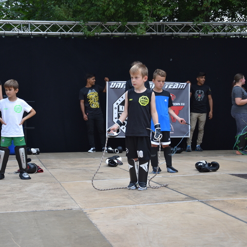 Gruppe von Kindern in Sportschuhen und Schutzausr&uuml;stung, die auf einem Platz mit Seilen und Boxhandschuhen trainieren.