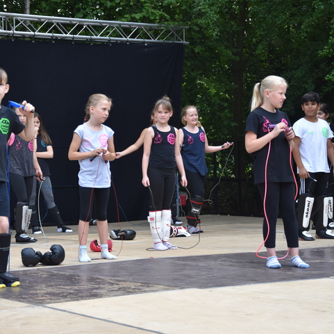 Gruppe von Kindern in Sportbekleidung auf einer B&uuml;hne, die mit Springseilen &uuml;ben. Hintergrund mit dunklem Vorhang.