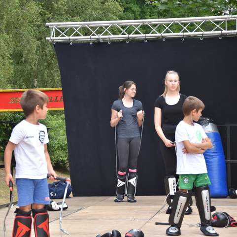 Vier Kinder und Jugendliche in Sportkleidung stehen auf einer Trainingsfl&auml;che mit Schutzausr&uuml;stung und einem Pratze.