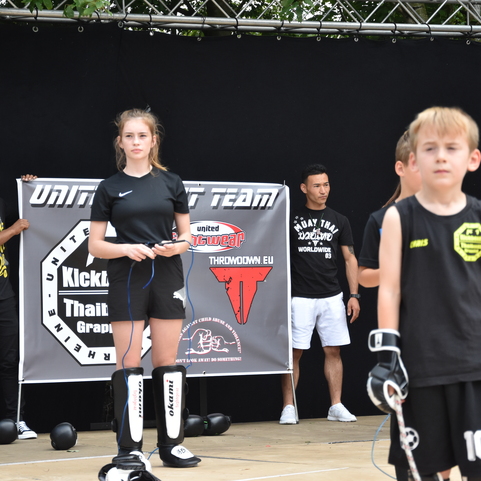 Gruppe junger Sportler auf einer Veranstaltung, mit einem Banner im Hintergrund, die verschiedene Kampfsportarten pr&auml;sentieren.