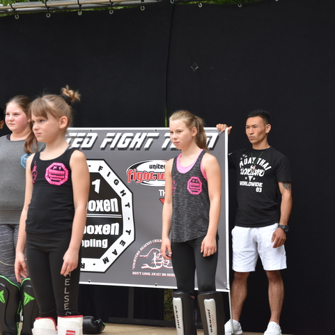 Gruppe von Sportlern bei einem Kampfsport-Event, mit einem Banner im Hintergrund und verschiedenen Trainingspositionen.