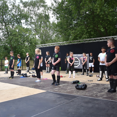 Gruppe von Kindern in Sportbekleidung steht auf einer B&uuml;hne und wartet auf den Beginn einer Veranstaltung im Freien.