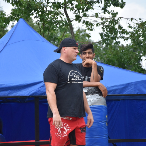 Drei M&auml;nner im Sportoutfit stehen unter einem blauen Zelt, im Hintergrund eine Frau mit Mikrofon und eine weitere Person.
