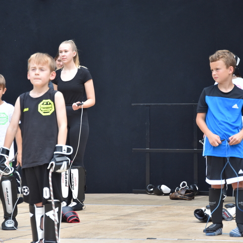 Gruppe von Kindern in Schutzausr&uuml;stung steht auf einer B&uuml;hne, bereit zu einer Sport&uuml;bung oder Vorf&uuml;hrung.