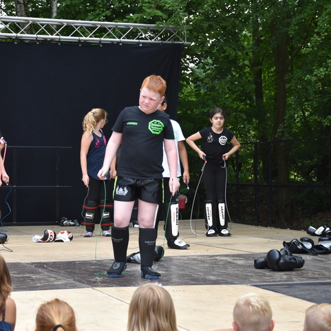 Kinder in schwarzen Trainingsanz&uuml;gen f&uuml;hren eine Vorf&uuml;hrung mit Seilspringen auf einer B&uuml;hne im Freien durch.