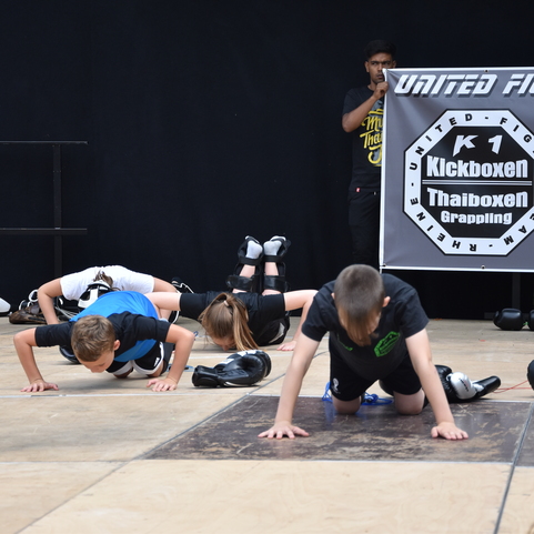 Mehrere Kinder f&uuml;hren Liegest&uuml;tze auf einem Trainingsboden unter einer Trainingsbanner durch.