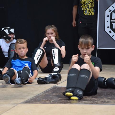 Vier Kinder in Sportausr&uuml;stung sitzen auf einer Trainingsfl&auml;che f&uuml;r Kickboxen und Thaiboxen.