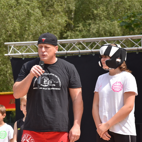 Ein Mann spricht zu einer Gruppe von Kindern, w&auml;hrend ein M&auml;dchen mit Schutzausr&uuml;stung daneben steht.