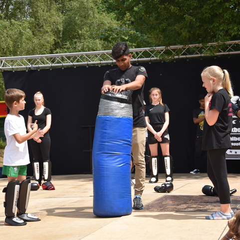 Gruppe von Kindern und Jugendlichen beobachtet einen Trainer, der eine Schlagpolstertechnik demonstriert.