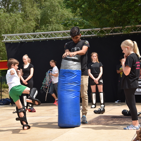 Kinder und Jugendliche trainieren an einem blauen Boxsack auf einer Freiluftb&uuml;hne.