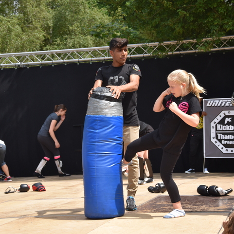 Kinder und Jugendliche &uuml;ben Kickbox-Techniken an einem blauen Boxsack unter Anleitung eines Trainers.