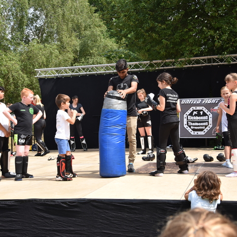 Kinder beobachten einen Trainer, der einen Kampfsport-Sack auf einer B&uuml;hne zur Demonstration vorbereitet.