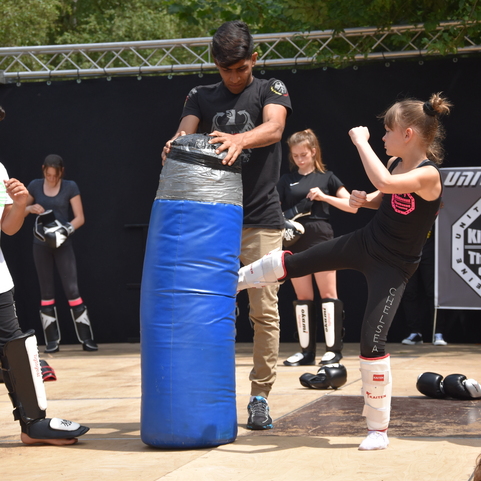 Kinder trainieren Kickboxen, w&auml;hrend ein Trainer mit einem blauen Boxsack arbeitet.