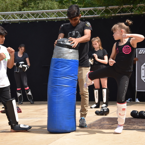 Jugendliche &uuml;ben Kickboxen auf einer Trainingsfl&auml;che mit einem blauen Boxsack und Schutzausr&uuml;stung.