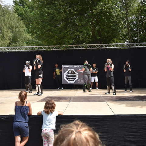 Gruppe von Sportlern in Boxhandschuhen trainiert auf einer Freiluftb&uuml;hne vor Zuschauern.