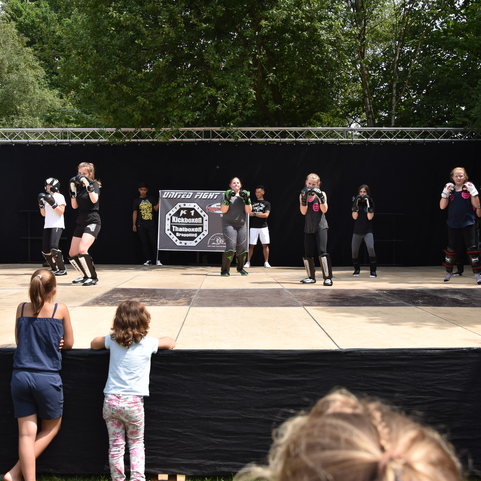 Gruppe von Kampfsportlern in Schutzausr&uuml;stung &uuml;bt auf einer B&uuml;hne, Zuschauer beobachten vom Rand.