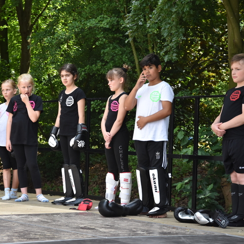 Sechs Kinder in Sportkleidung stehen in einem Park, bereit f&uuml;r ein Training im Kampfsport.