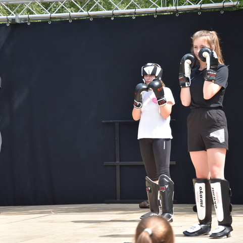 Drei Jugendliche in Schwarz tragen Boxhandschuhe und sind auf einer B&uuml;hne zum Training in Boxhaltung bereit.