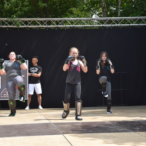 Vier M&auml;dchen in Sportkleidung f&uuml;hren Kickboxbewegungen auf einer B&uuml;hne vor einem schwarzen Hintergrund aus.