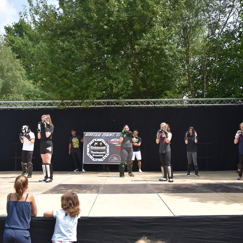 Gruppentraining mit mehreren Personen in Sportkleidung auf einer Freiluftb&uuml;hne, Umstehenden zuschauend.