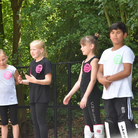 Vier Kinder stehen an einem Zaun, zwei tragen Schutzausr&uuml;stung, w&auml;hrend sie miteinander kommunizieren.