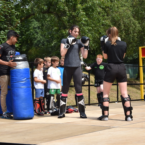 Zwei Frauen trainieren im Boxen auf einer B&uuml;hne, umgeben von Zuschauern und einem Trainingsdummy.