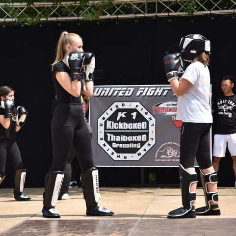 Zwei junge Frauen im Box-Outfit stehen sich gegen&uuml;ber und trainieren Kickboxen auf einer Wettkampf-B&uuml;hne.