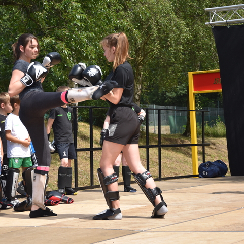 Zwei Frauen trainieren Muay Thai auf einer Au&szlig;enb&uuml;hne, Zuschauer beobachten das Geschehen.