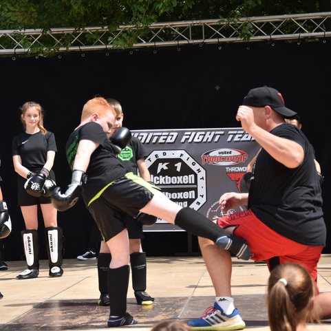 Jugendliche in Kampfsportausr&uuml;stung f&uuml;hren Techniken auf einer Trainingsfl&auml;che mit schwarzem Hintergrund vor.