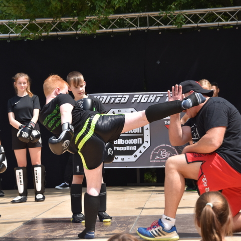 Kinder trainieren in Schwarz-Gelb beim Kickboxen auf einer Trainingsb&uuml;hne, ein Trainer zeigt ihnen eine Technik.