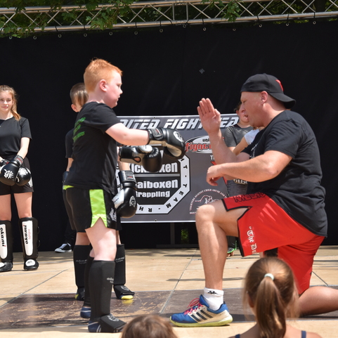 Junge &uuml;bt mit Trainer Boxtechniken auf einer Trainingsfl&auml;che; Zuschauer beobachten.