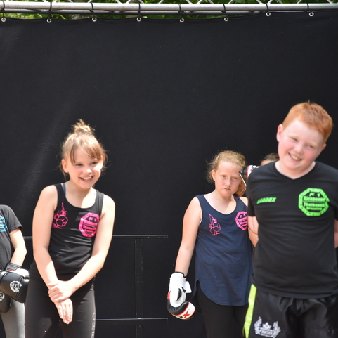 Gruppe von Kindern in Sportkleidung, l&auml;chelnd und stehend vor einem schwarzen Hintergrund.