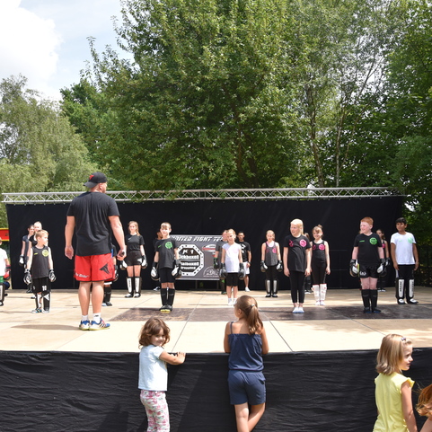 Kinder in schwarzen Outfits f&uuml;hren eine Tanzprobe auf einer B&uuml;hne unter Anleitung eines Trainers durch.