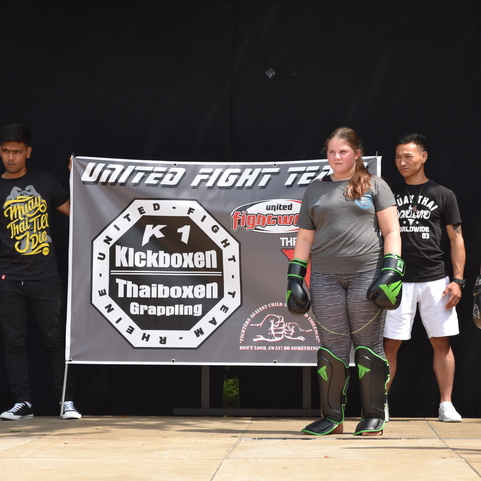 Gruppentraining im Kampfsport mit Teilnehmern in Schutzausr&uuml;stung vor einem Banner mit &bdquo;United Fight Team&ldquo;.