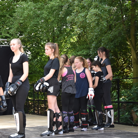 Gruppe von Kindern und Jugendlichen in Sportkleidung mit Boxhandschuhen, die auf einer Trainingsb&uuml;hne warten.