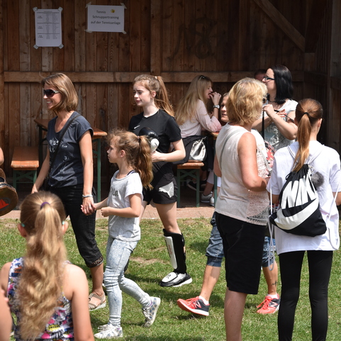 Gruppiertes Zusammensein von Menschen auf einer Wiese, einige tragen Sportbekleidung und unterhalten sich.