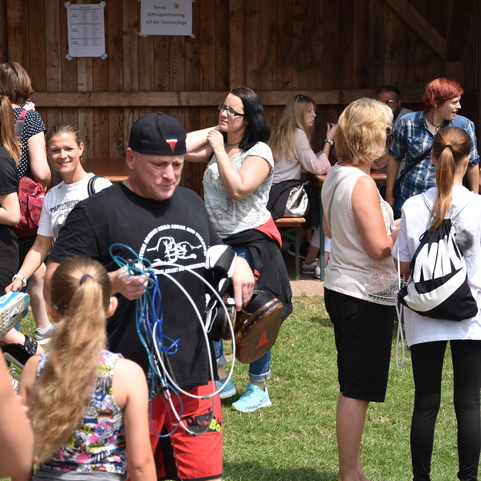 Menschen in sportlicher Kleidung versammeln sich auf einer Wiese, einige unterhalten sich, andere tragen Ausr&uuml;stung.