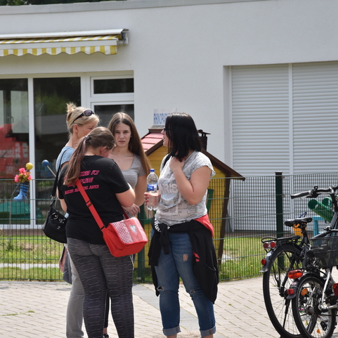 Vier Frauen stehen im Gespr&auml;ch vor einem Spielplatz; im Hintergrund sind Fahrr&auml;der und eine Kinderspielecke sichtbar.