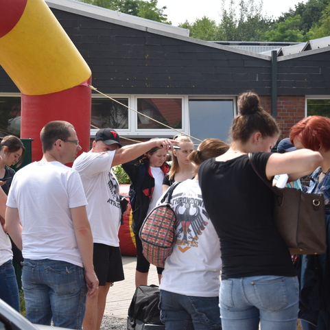 Gruppe von Menschen steht in einer Warteschlange vor einem bunten Eingang zu einem Festgel&auml;nde.