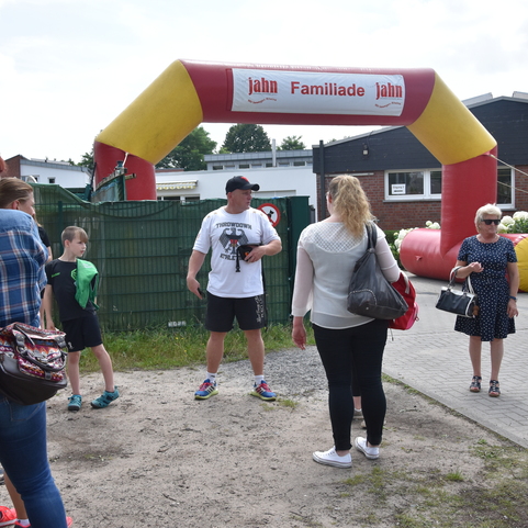 Familienfest-Eingang mit roten und gelben Luftb&ouml;gen; mehrere Erwachsene und Kinder unterhalten sich davor.