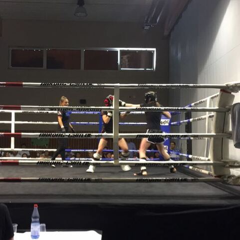 Zwei Boxer im Ring w&auml;hrend eines Kampfes, w&auml;hrend ein Kameramann das Geschehen filmt. Zuschauer im Hintergrund.