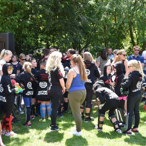Gruppe von Kindern in Schwarz mit Schutzausr&uuml;stung stehen auf einer Wiese, umringt von Zuschauern.