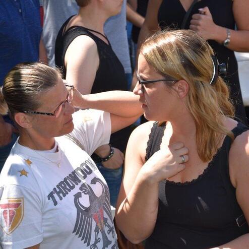 Zwei Frauen stehen im Gespr&auml;ch auf einer Versammlung, umgeben von anderen Teilnehmern im Hintergrund.