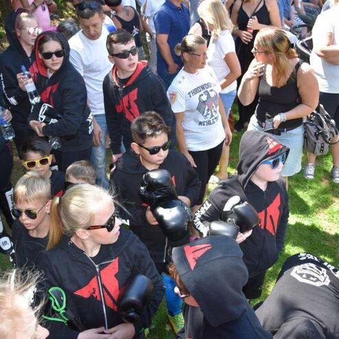 Gruppe von Kindern in schwarzen Kapuzenpullis mit Boxhandschuhen und Sonnenbrillen, umgeben von Zuschauern im Freien.